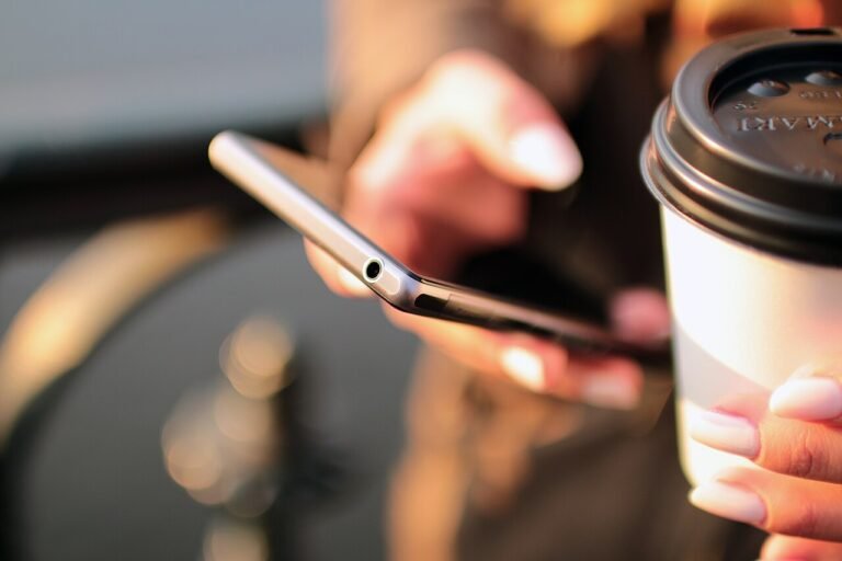 Hands holding a smartphone beside a takeaway coffee cup.